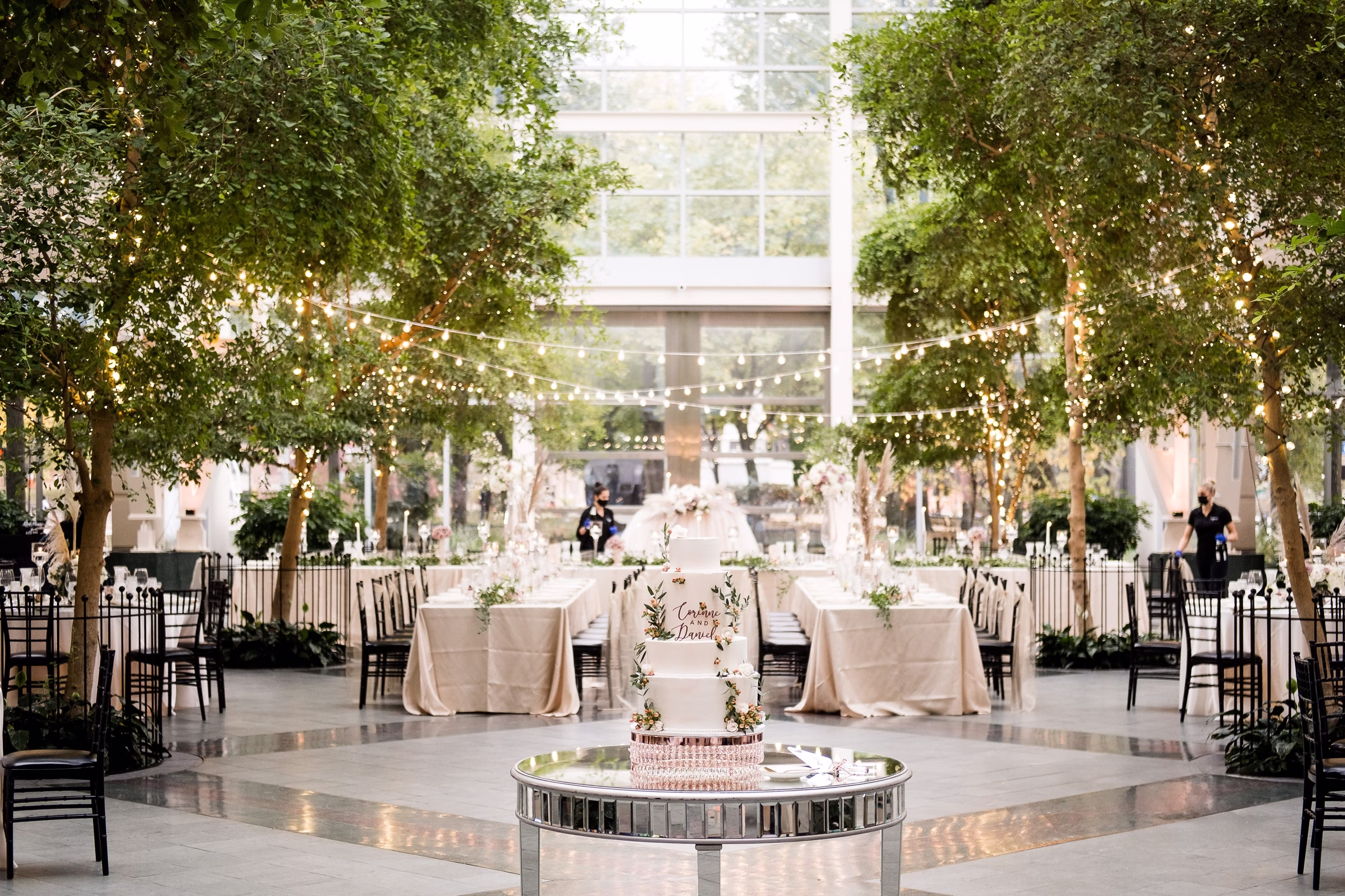Elegant wedding reception with string lights overhead, round mirrored cake table, and neutral linens designed by luxury event designer Erin McDonald