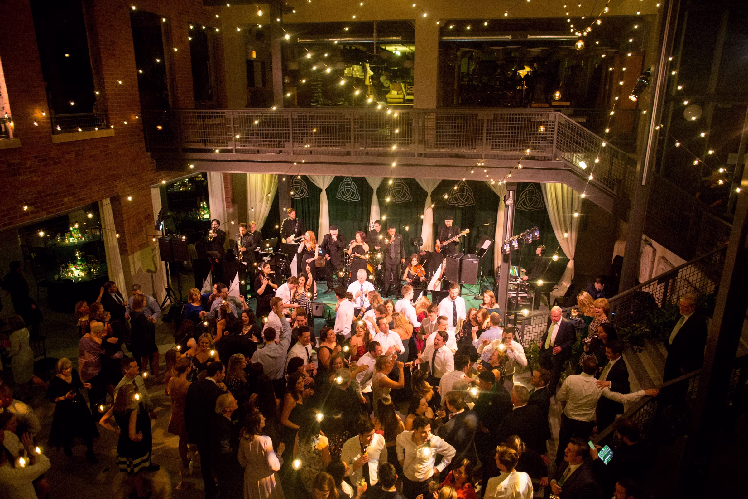 Luxury wedding reception with live band performance and guests dancing in elegant venue with string lights overhead in Chicago