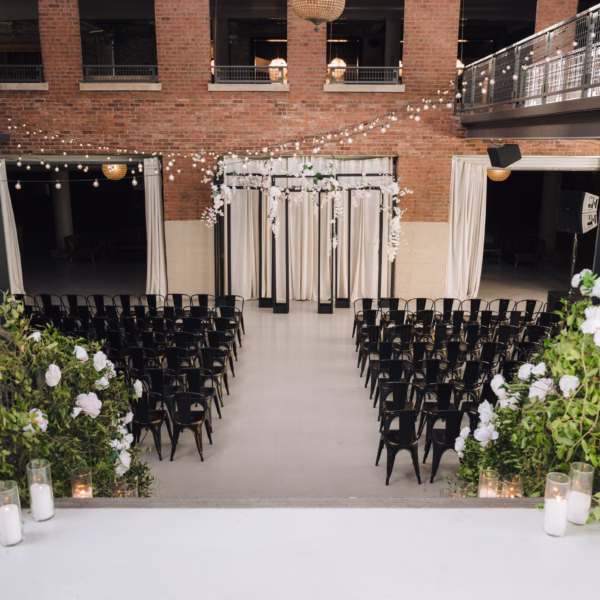 Industrial Chicago wedding ceremony space with black chairs, white floral arrangements, string lights and brick architecture designed by Erin McDonald