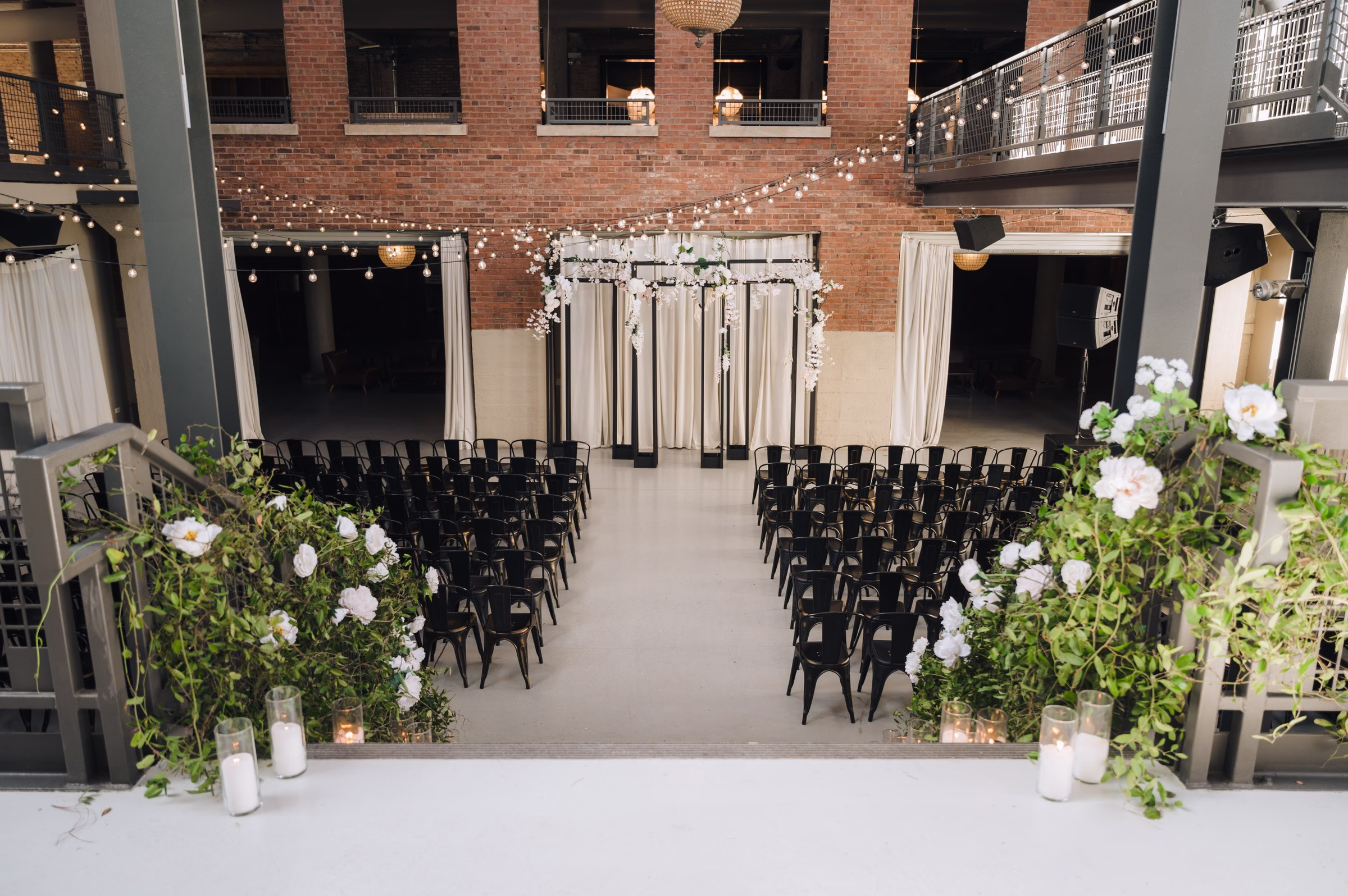 Industrial Chicago wedding ceremony space with black chairs, white floral arrangements, string lights and brick architecture designed by Erin McDonald