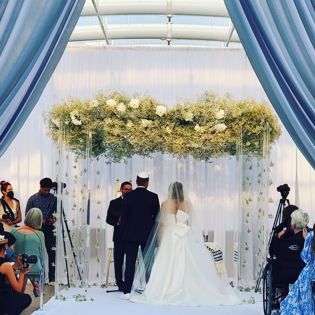 Elegant wedding ceremony under floral chuppah with greenery and white roses designed by Chicago wedding designer Erin McDonald
