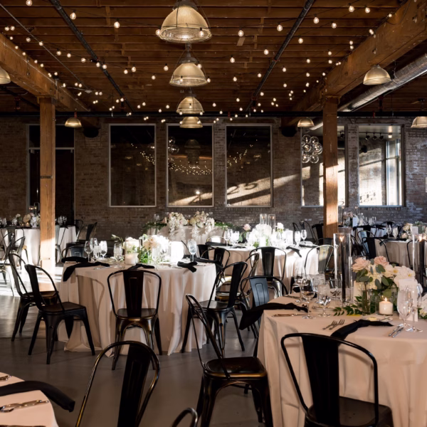 Elegant Chicago wedding reception in industrial venue with ivory linens, black metal chairs, and string lights designed by Erin McDonald