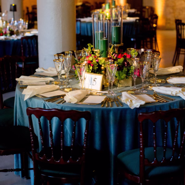 Elegant wedding reception table with blue linens, gold chargers, crystal glassware and green candle centerpiece designed by Erin McDonald in Chicago