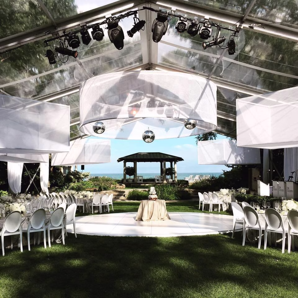 Elegant outdoor wedding ceremony setup under clear tent with white chairs and ocean view designed by Erin McDonald