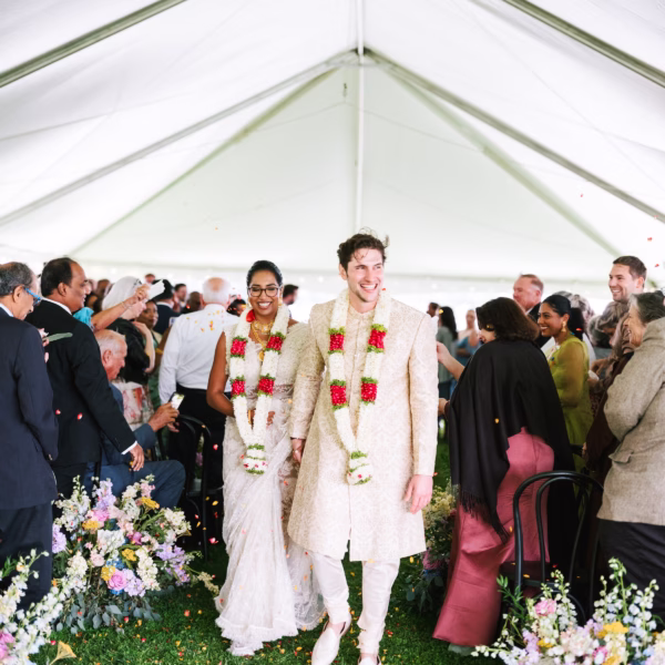 Newlyweds walking down aisle after Indian fusion wedding ceremony under white tent with floral arrangements designed by destination wedding designer Erin McDonald