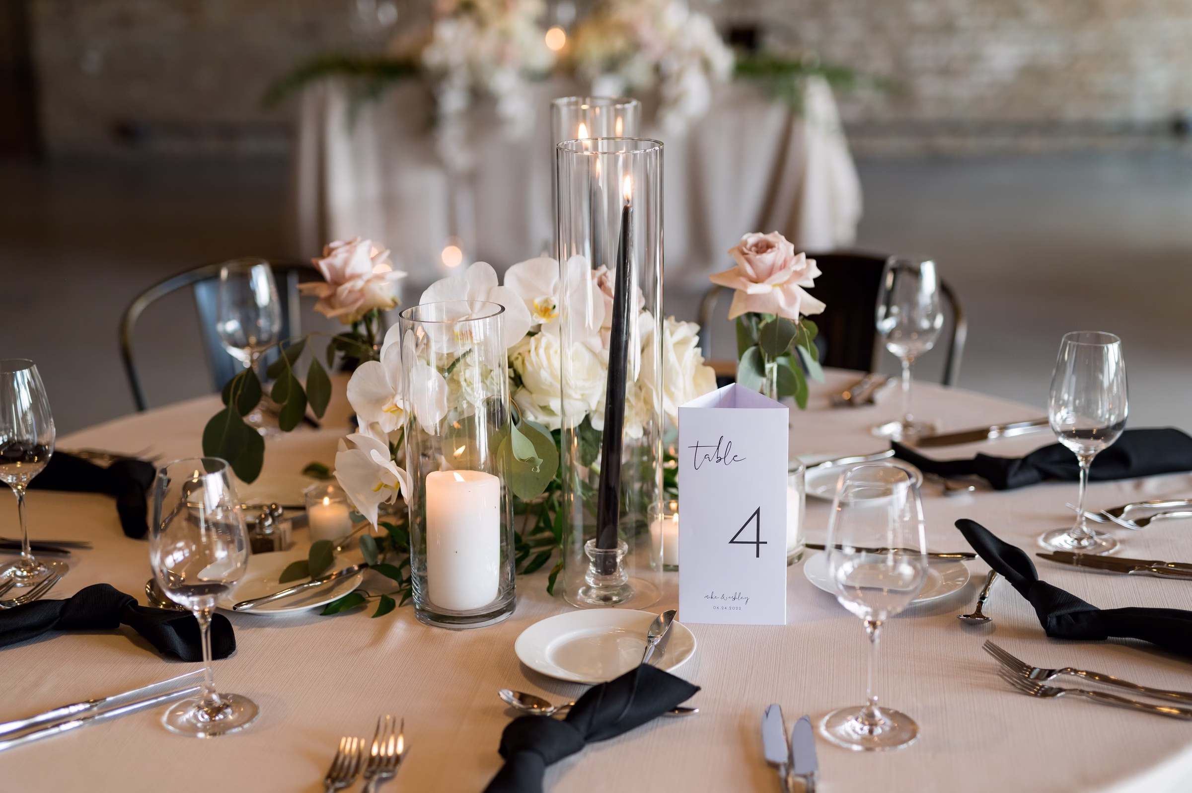 Elegant wedding reception table centerpiece with white and blush roses, tall taper candles in glass cylinders, and table number 4 designed by Chicago wedding designer Erin McDonald