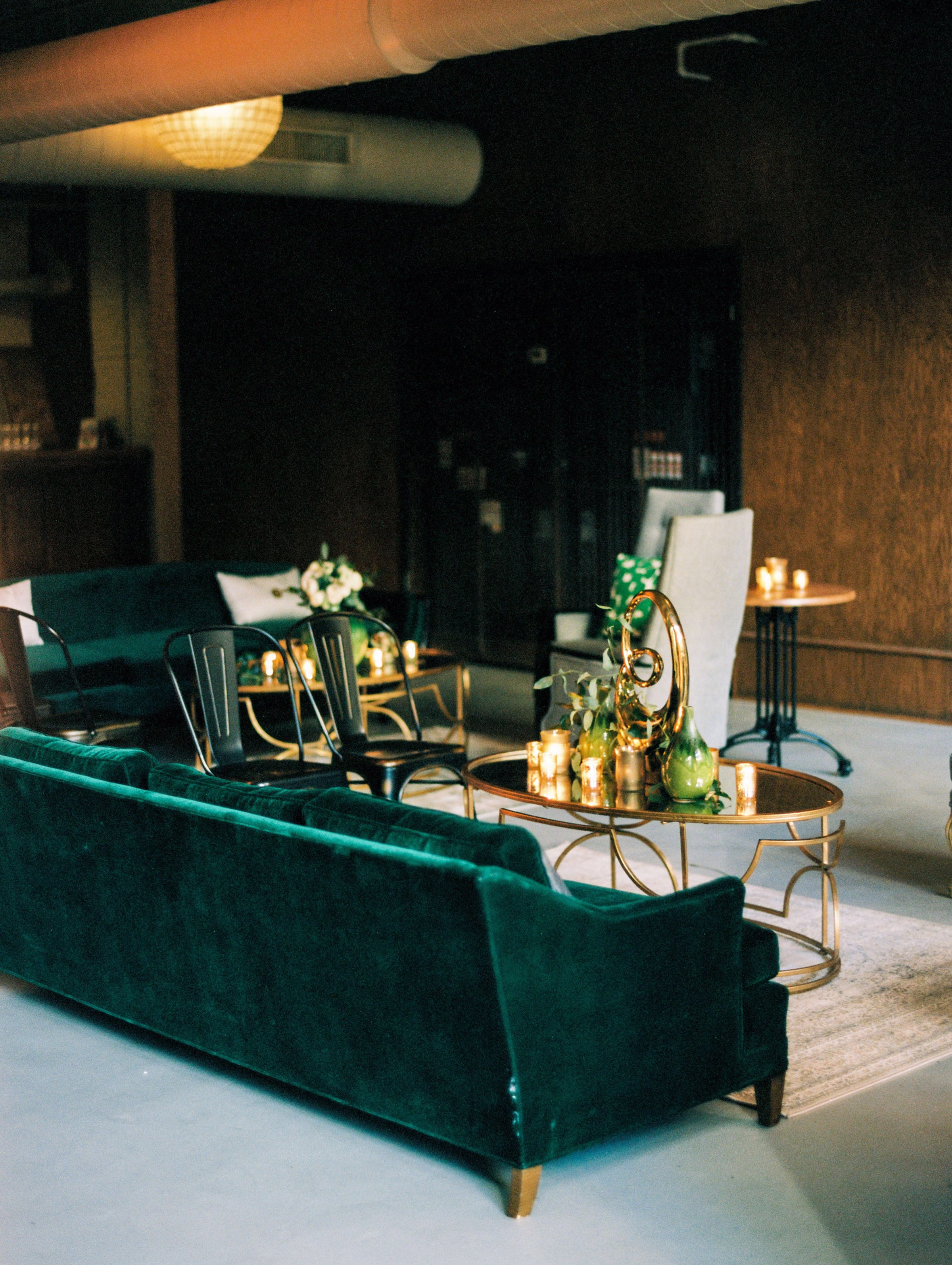 Luxurious emerald green velvet sofas with gold accent tables and candles create an elegant cocktail lounge designed by Chicago wedding planner Erin McDonald