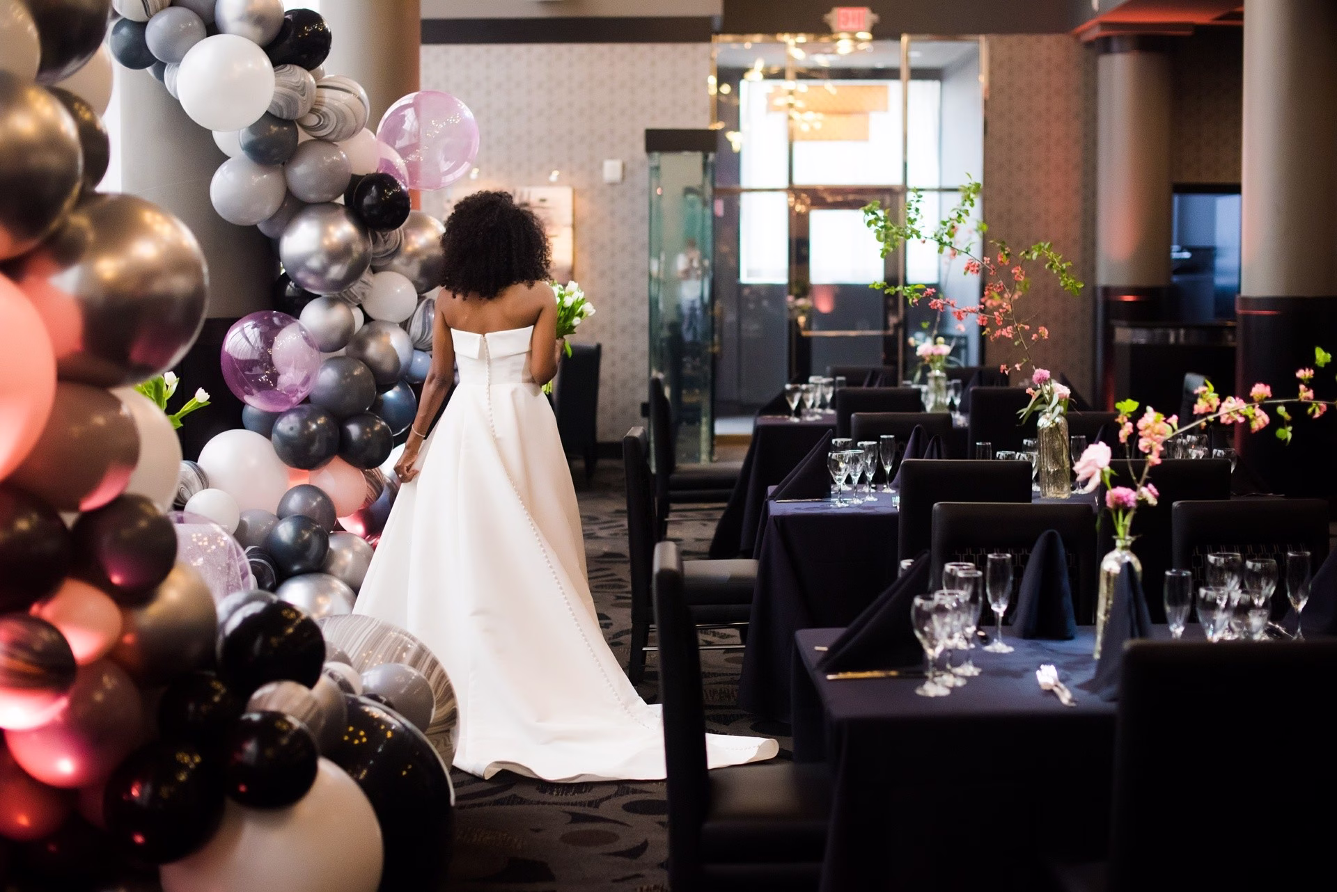 Bride in white gown stands beside elaborate balloon installation