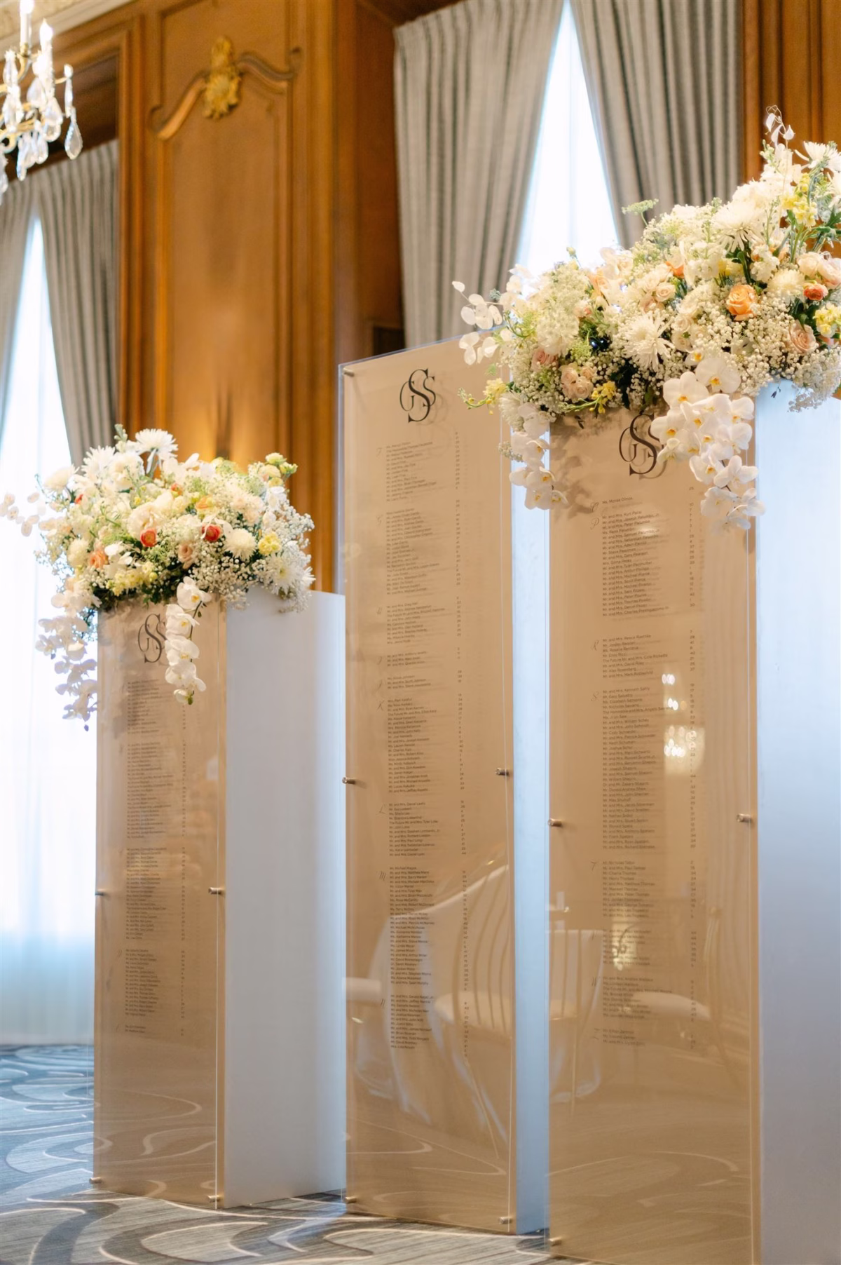 Elegant acrylic seating chart displays with white floral arrangements designed by Erin McDonald in luxurious ballroom setting
