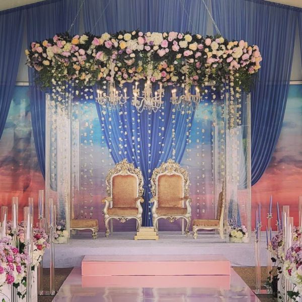 Elegant South Asian wedding ceremony setup with ornate golden chairs, crystal chandelier, cascading floral ceiling installation and blue draping designed by Erin McDonald