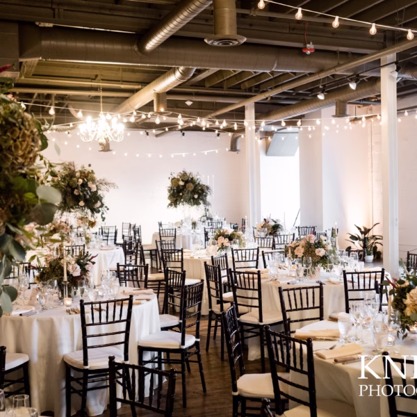 Industrial wedding reception with string lights, elegant floral centerpieces, and Chiavari chairs designed by Erin McDonald