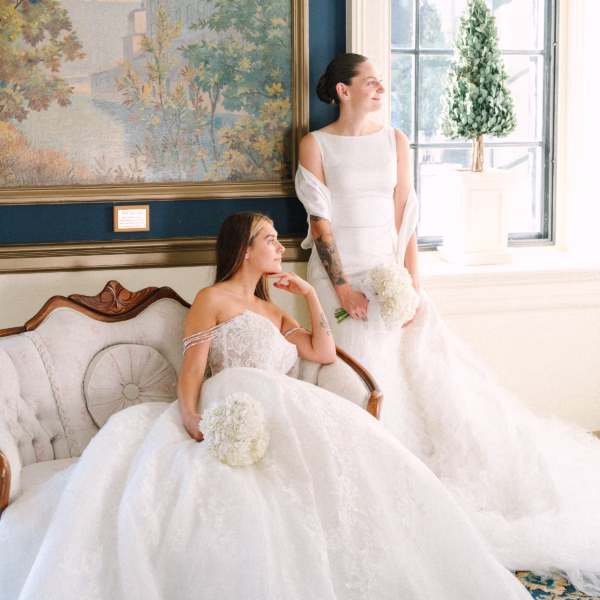Two brides in elegant wedding gowns pose for portraits in the luxurious parlor room at Inn on Broadway in Rochester NY, coordinated by wedding designer Erin McDonald