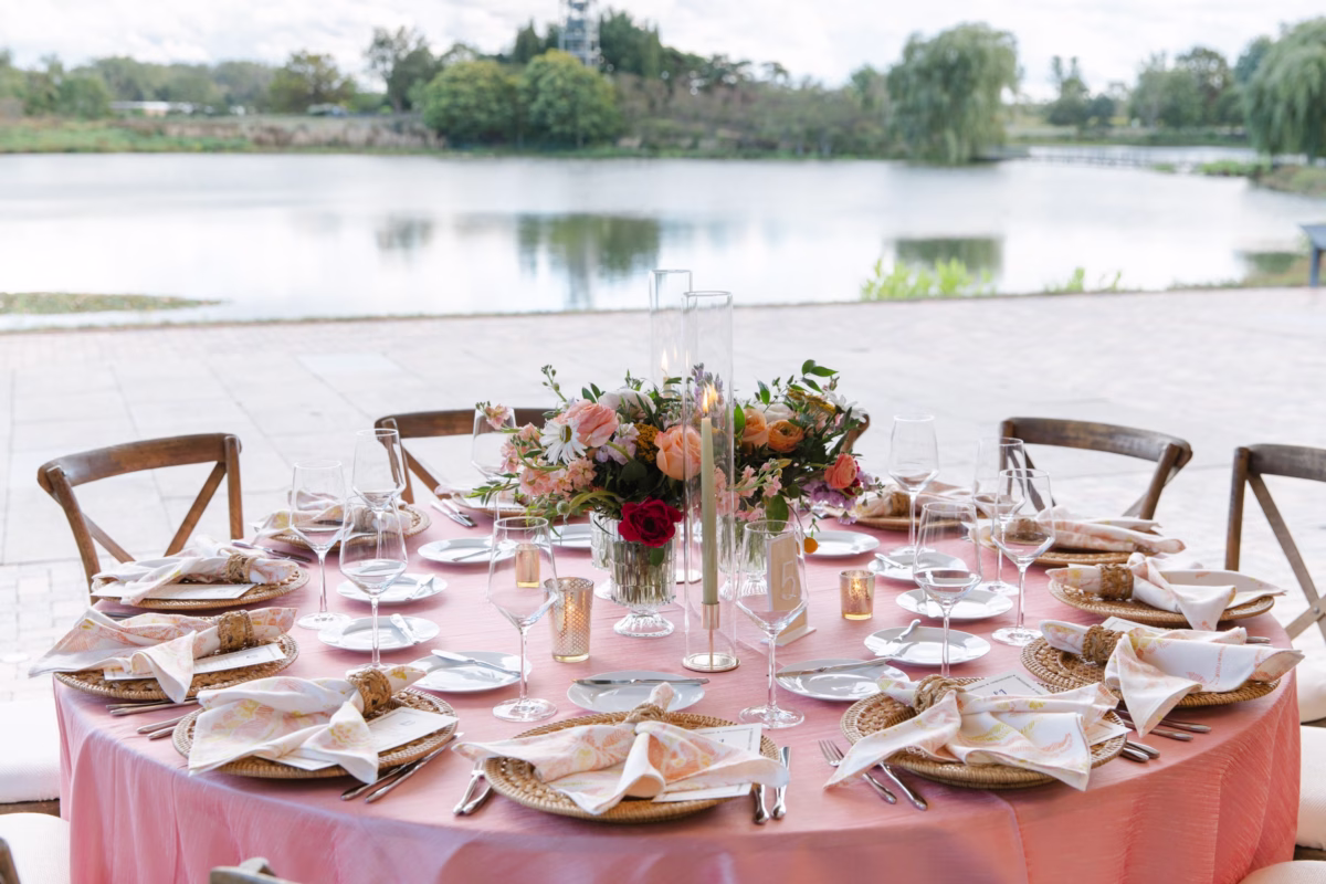 wedding designer waterfront reception tablescape - Destination Event Design Elegant pink waterfront wedding reception tablescape designed by Erin McDonald featuring coral floral centerpieces and rattan chargers overlooking a serene lake