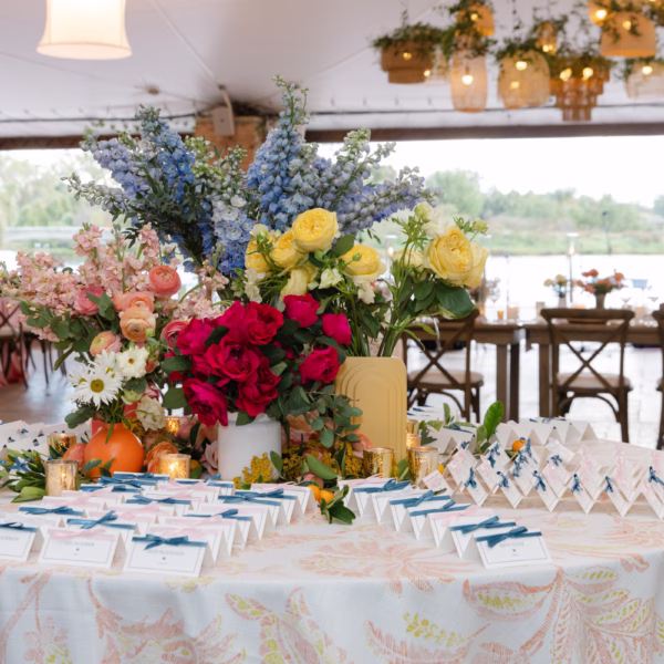 Elegant escort card table with vibrant floral centerpiece featuring blue delphinium, red roses, and yellow blooms at wedding designed by Erin McDonald