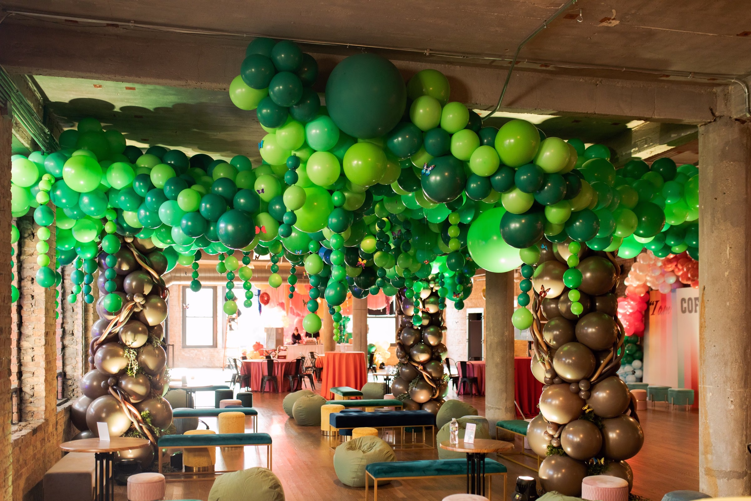 Elaborate green balloon canopy installation with brown tree trunk columns