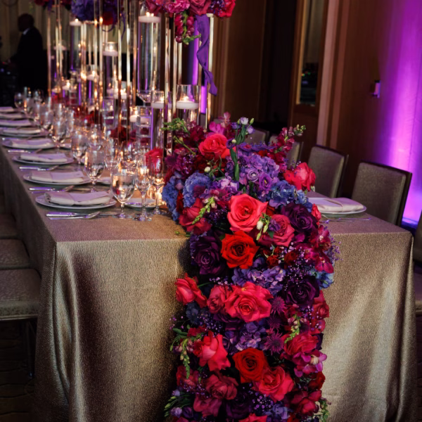 Luxurious purple and red floral garland table runner with tall glass candle centerpieces