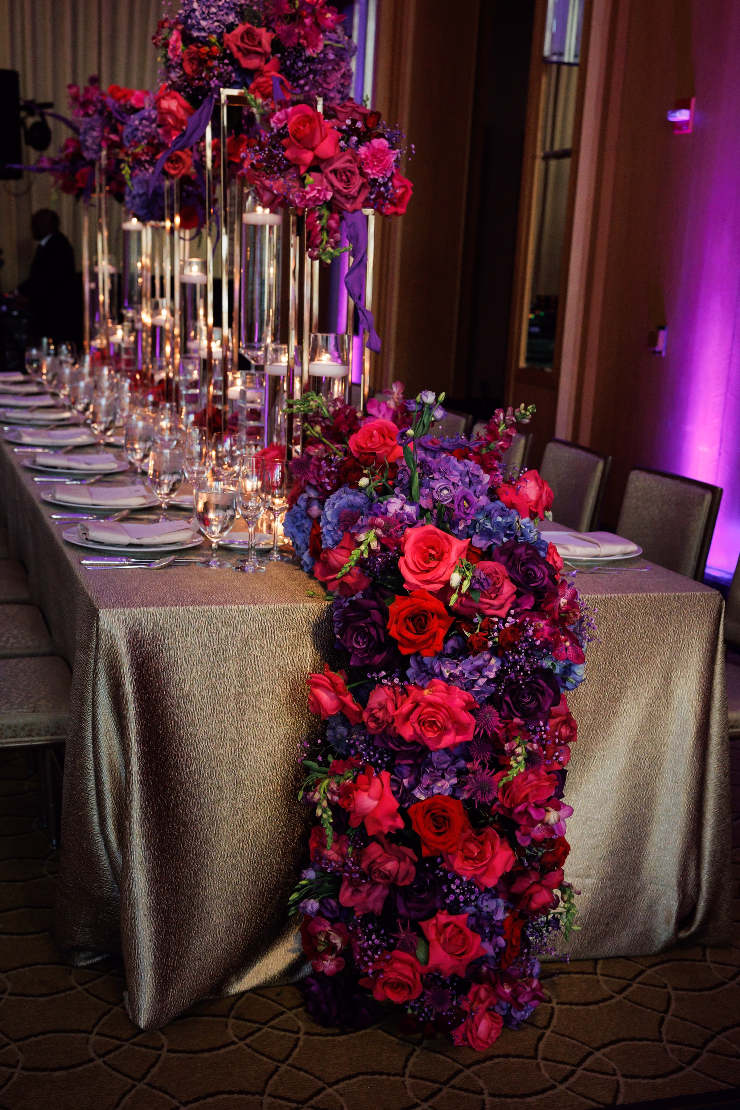 Luxurious purple and red floral garland table runner with tall glass candle centerpieces