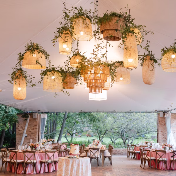 Elegant wedding reception tent featuring suspended wicker basket chandeliers with greenery and coral linens