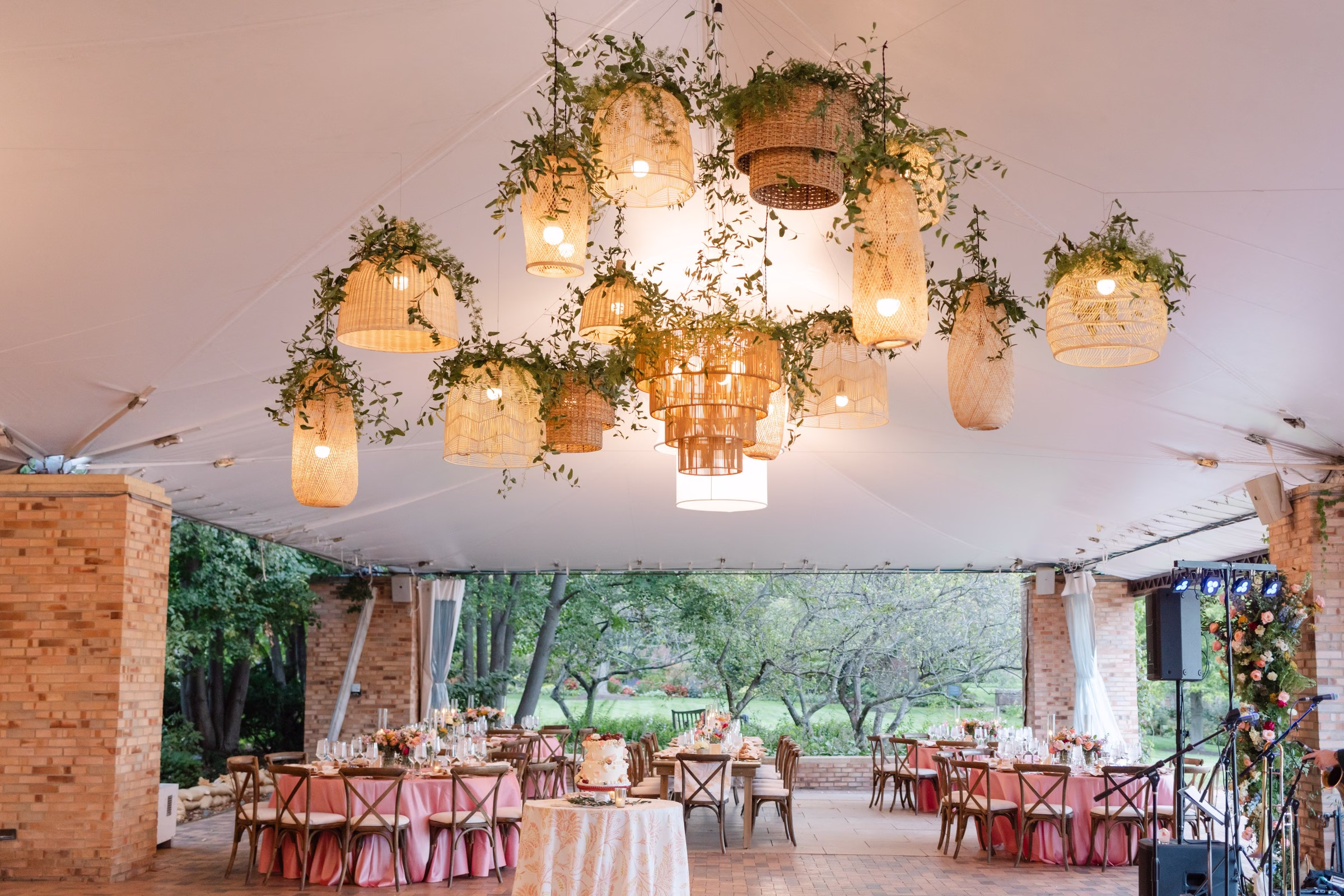Elegant wedding reception tent featuring suspended wicker basket chandeliers with greenery and coral linens