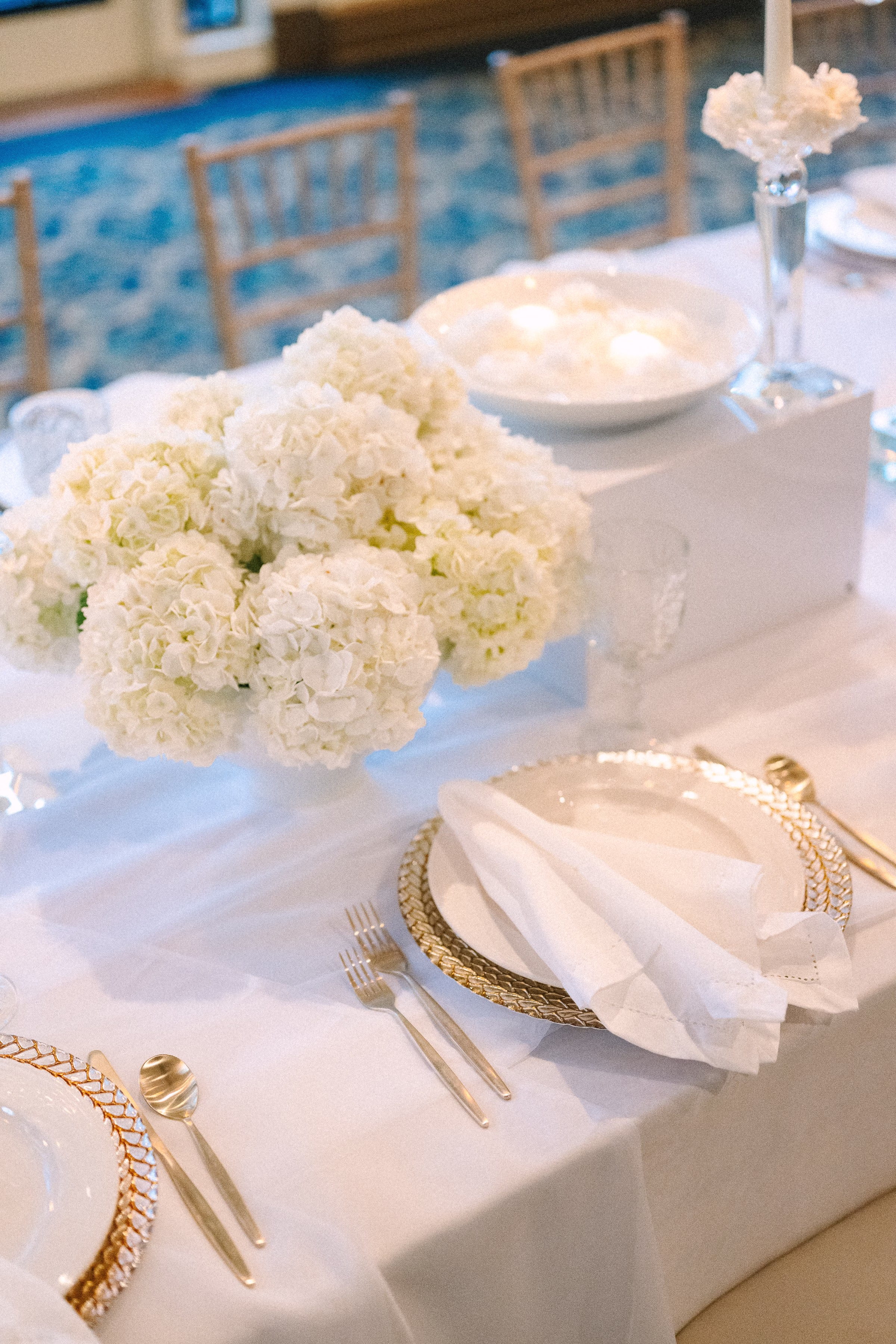 Elegant white and neutral wedding tablescape with gold charger plates and white floral centerpieces